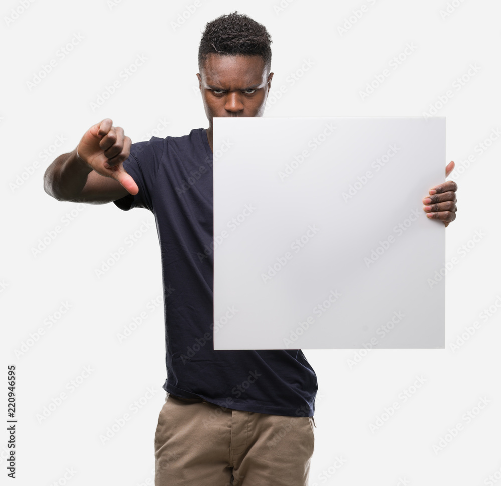 Young african american man holding a banner with angry face, negative sign showing dislike with thumbs down, rejection concept Young african american man holding a banner with angry face, negative sign showing dislike with thumbs down, rejection concept