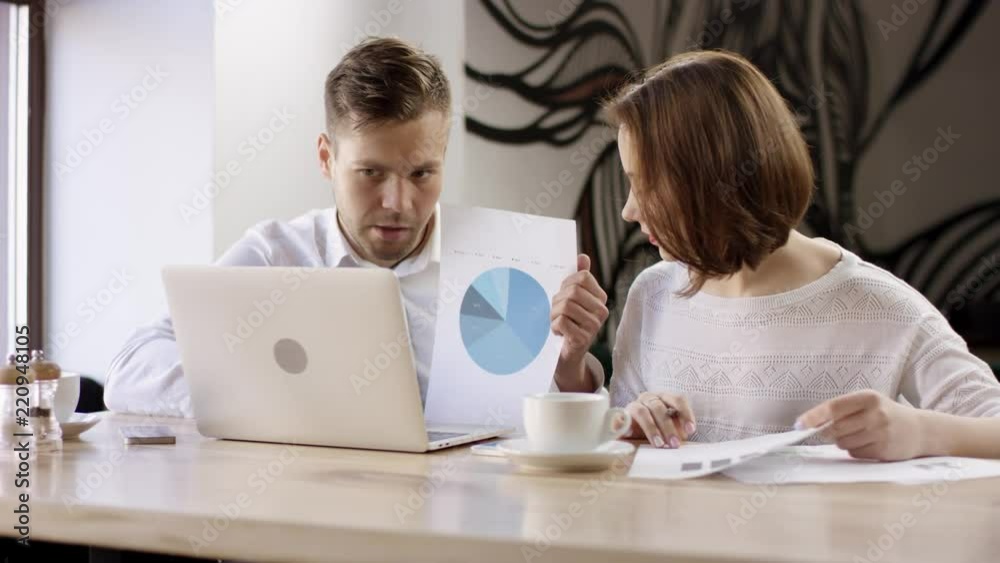 Two young people work with a laptop in a cafe. They are discussing and preparing the contract. It is a business meeting. Man and woman are sitting in the cafe at the table during break. Couple are Two young people work with a laptop in a cafe. They are discussing and preparing the contract. It is a business meeting. Man and woman are sitting in the cafe at the table during break. Couple are