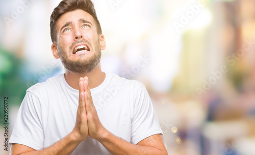 Young handsome man over isolated background begging and praying with hands together with hope expression on face very emotional and worried. Asking for forgiveness. Religion concept.