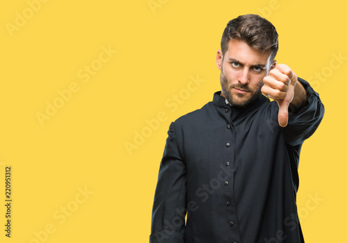 Young catholic christian priest man over isolated background looking unhappy and angry showing rejection and negative with thumbs down gesture. Bad expression.