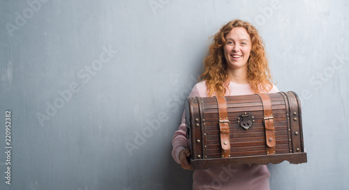Cuadro en lienzo Young redhead woman holding vintage chest with a happy face standing and smiling