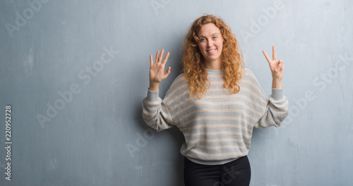 Young redhead woman over grey grunge wall showing and pointing up with fingers number seven while smiling confident and happy.