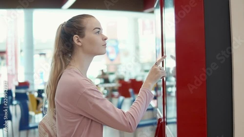 Young blonde girl ordering food in fast food restaurant using self-service payment machine, self-service kiosk. Consumer using technologies to buy food.