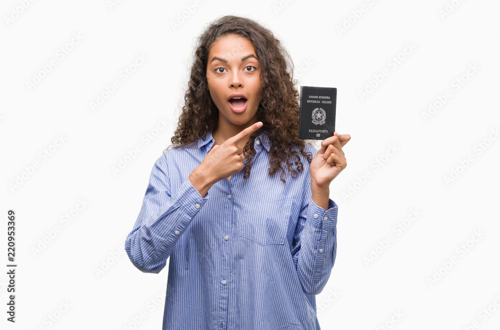 Young hispanic woman holding passport of Italy very happy pointing with hand and finger Young hispanic woman holding passport of Italy very happy pointing with hand and finger