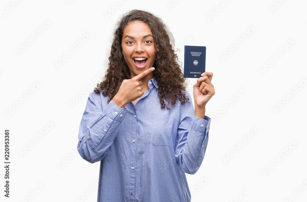 Young hispanic woman holding passport of Germany very happy pointing with hand and finger Young hispanic woman holding passport of Germany very happy pointing with hand and finger