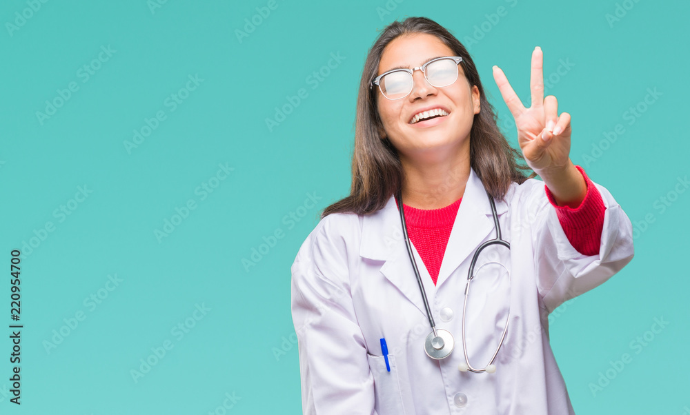 Young arab doctor woman over isolated background smiling looking to the camera showing fingers doing victory sign. Number two. Young arab doctor woman over isolated background smiling looking to the camera showing fingers doing victory sign. Number two.
