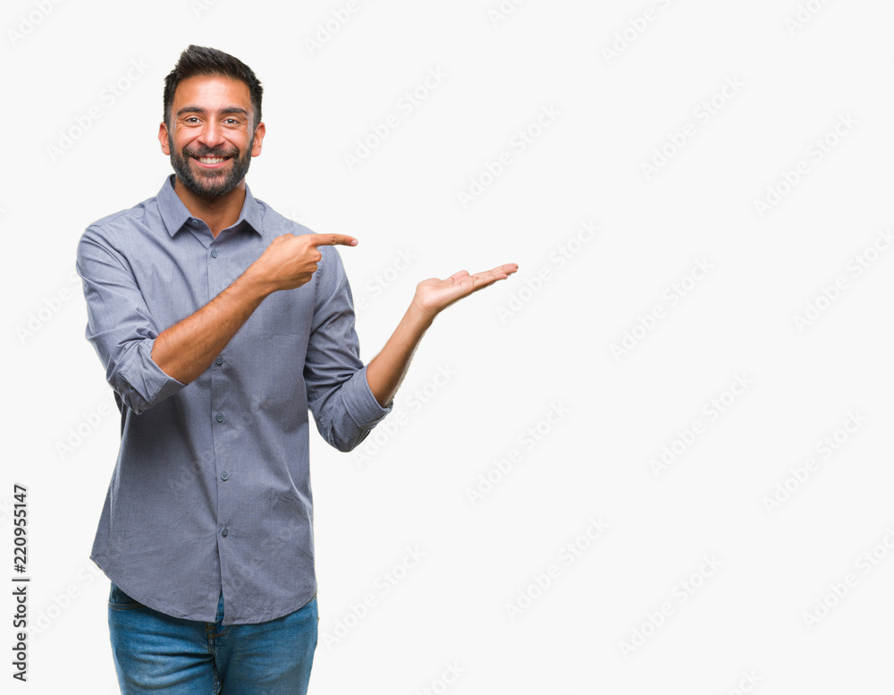Adult hispanic man over isolated background amazed and smiling to the camera while presenting with hand and pointing with finger. Adult hispanic man over isolated background amazed and smiling to the camera while presenting with hand and pointing with finger.