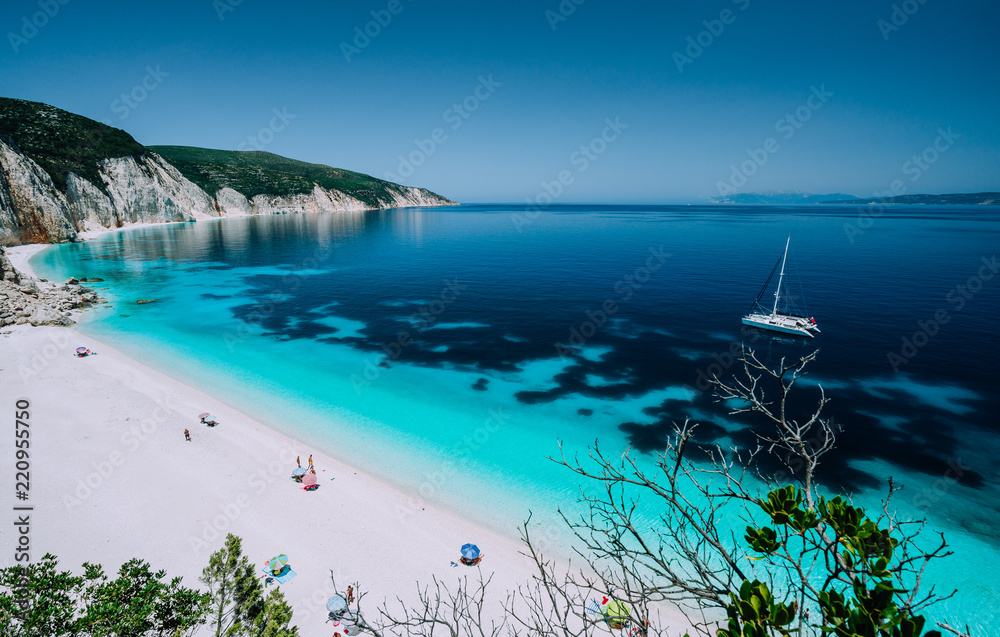 Panoramic view to remote beach wiht lonely white catamaran yacht drift in clear blue Caribbean like sea water. Tourists leisure activity on the beach with azure colored shallow lagoon