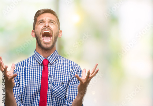 Young handsome business man over isolated background crazy and mad shouting and yelling with aggressive expression and arms raised. Frustration concept.