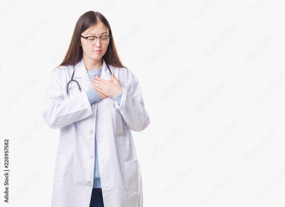 Young Chinese doctor woman over isolated background smiling with hands on chest with closed eyes and grateful gesture on face. Health concept. Young Chinese doctor woman over isolated background smiling with hands on chest with closed eyes and grateful gesture on face. Health concept.