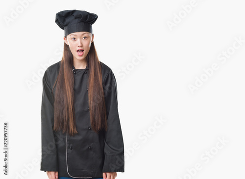 Young Chinese woman over isolated background wearing chef uniform afraid and shocked with surprise expression, fear and excited face.