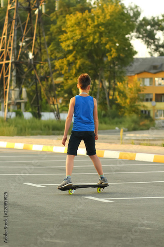 Boy riding skate board on summer parking lot near power station, back view, sunset