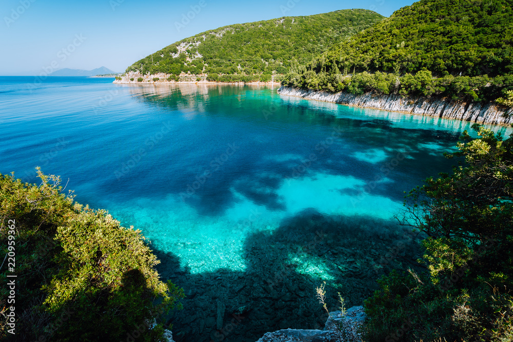 Azure bay. Picturesque scenery of the cove with turquoise calm water, surrounded by hills with cypresses, pine and olive trees. White limestone cliffs mirrow in the crystal clear water