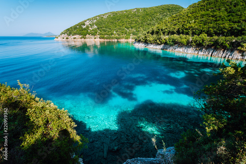 Azure bay. Picturesque scenery of the cove with turquoise calm water, surrounded by hills with cypresses, pine and olive trees. White limestone cliffs mirrow in the crystal clear water