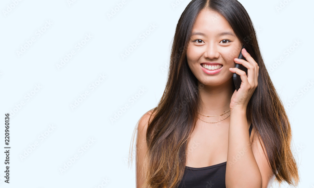 Young asian woman speaking on the phone over isolated background with a happy face standing and smiling with a confident smile showing teeth Young asian woman speaking on the phone over isolated background with a happy face standing and smiling with a confident smile showing teeth
