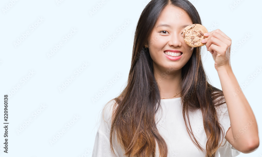 Young asian woman eating chocolate chip cookie over isolated background with a happy face standing and smiling with a confident smile showing teeth Young asian woman eating chocolate chip cookie over isolated background with a happy face standing and smiling with a confident smile showing teeth