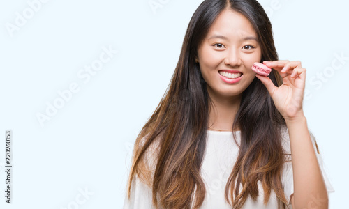 Young asian woman eating pink macaron sweet over isolated background with a happy face standing and smiling with a confident smile showing teeth
