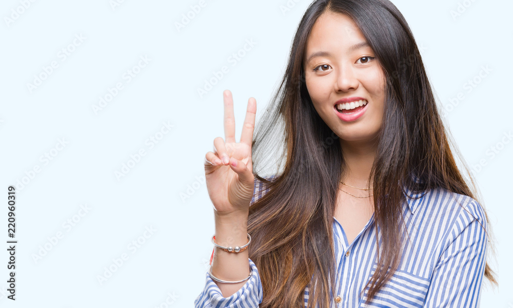 Young asian woman over isolated background smiling with happy face winking at the camera doing victory sign. Number two. Young asian woman over isolated background smiling with happy face winking at the camera doing victory sign. Number two.