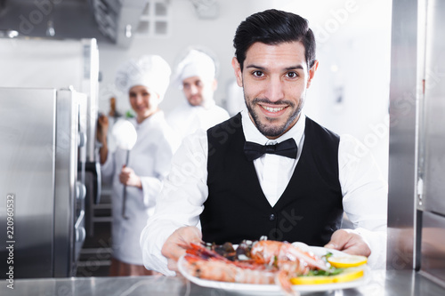 Waiter with dish of seafood in kitchen on restaurant