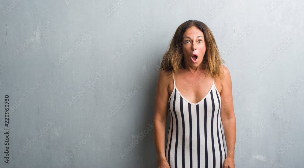 Middle age hispanic woman standing over grey grunge wall scared in shock with a surprise face, afraid and excited with fear expression Middle age hispanic woman standing over grey grunge wall scared in shock with a surprise face, afraid and excited with fear expression