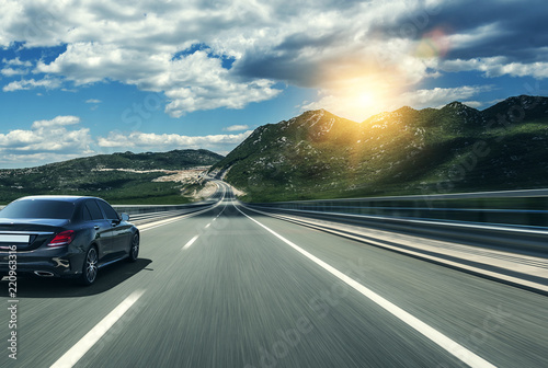Black car rushing along a high-speed highway in the sun. © Denis Rozhnovsky