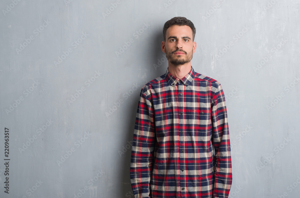 Fototapeta premium Young adult man standing over grey grunge wall with a confident expression on smart face thinking serious