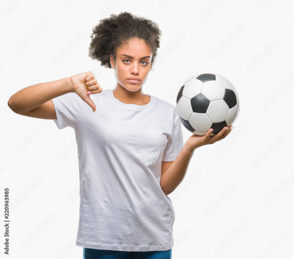 Young beautiful afro american holding soccer football ball over isolated background with angry face, negative sign showing dislike with thumbs down, rejection concept Young beautiful afro american holding soccer football ball over isolated background with angry face, negative sign showing dislike with thumbs down, rejection concept