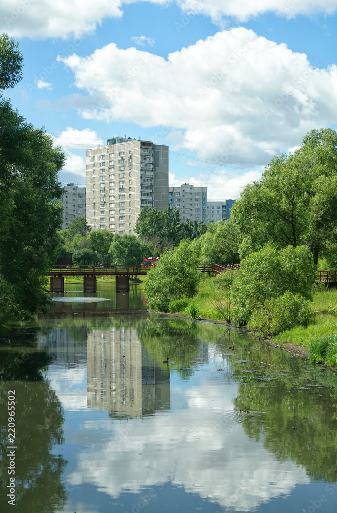 Reflection of clouds in the water. River chertyanka and a natural park on the background of residential buildings in Moscow.