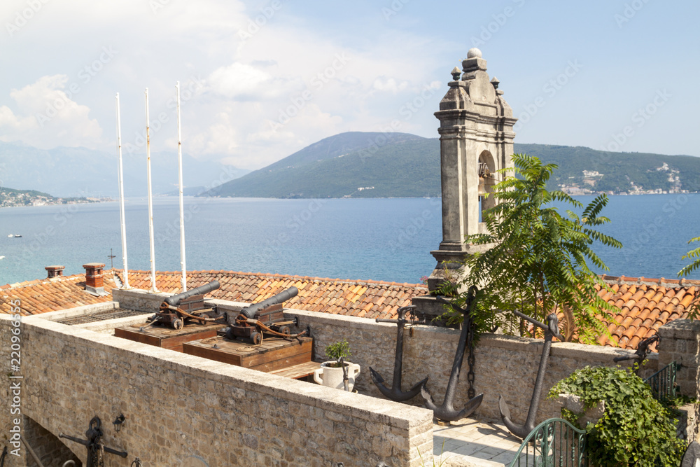 Ancient anchors and cannons stored in the Maritime Museum, an old bell tower and a stunning view of the Bay of Kotor behind it