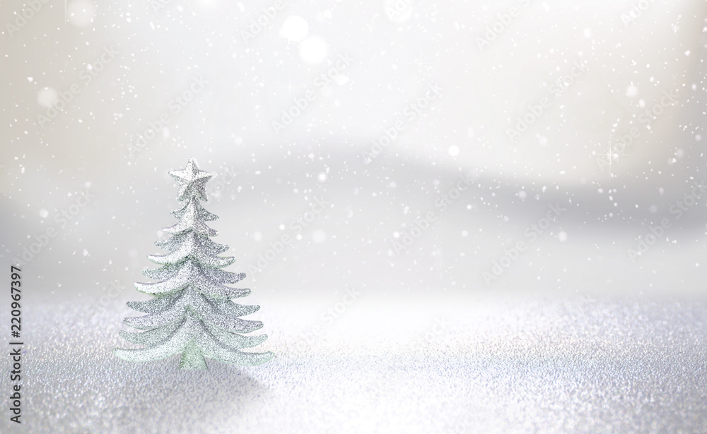 Winter christmas scenic background. Silvery small Christmas tree on a blurred snowy defocused background in pearl silver tones with copy space.