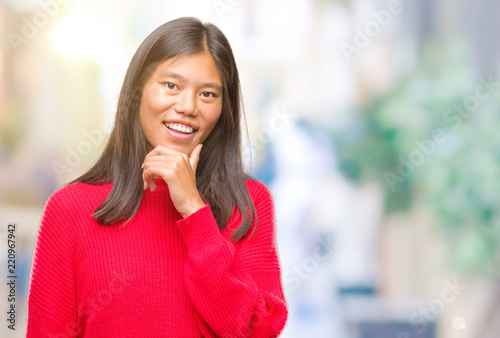 Young asian woman wearing winter sweater over isolated background looking confident at the camera with smile with crossed arms and hand raised on chin. Thinking positive.