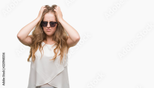 Young blonde woman wearing sunglasses suffering from headache desperate and stressed because pain and migraine. Hands on head. © Krakenimages.com