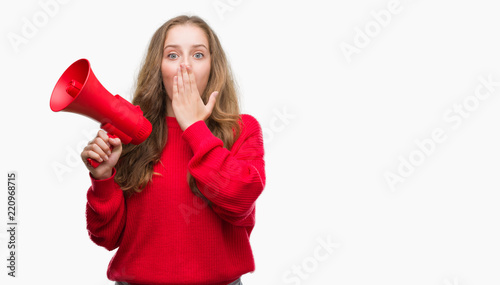 Young blonde woman holding red megaphone cover mouth with hand shocked with shame for mistake, expression of fear, scared in silence, secret concept