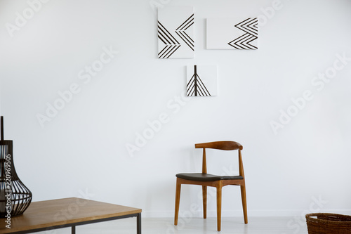 Posters on white wall above wooden chair in minimal living room interior with table. Real photo