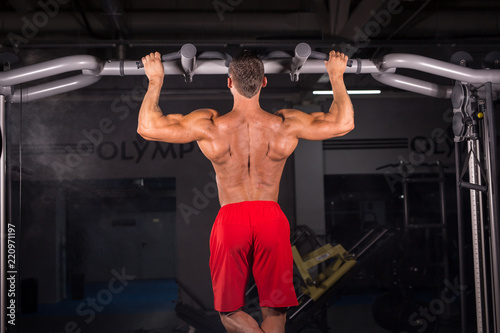 Strong young man doing pull up exercise on horizontal bar in gym