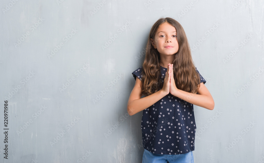 Young hispanic kid over grunge grey wall praying with hands together asking for forgiveness smiling confident. Young hispanic kid over grunge grey wall praying with hands together asking for forgiveness smiling confident.