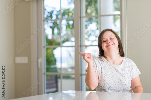 Down syndrome woman at home very happy pointing with hand and finger to the side