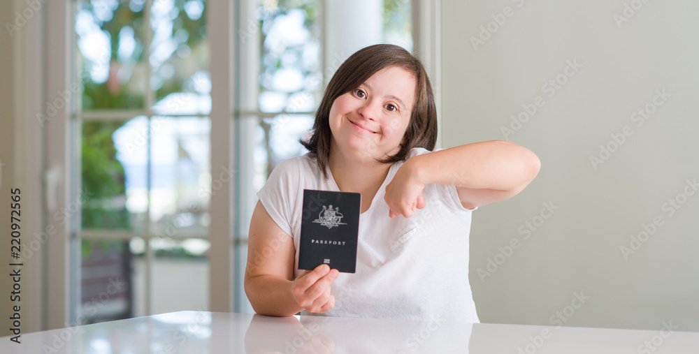 Down syndrome woman at home holding australian passport with surprise face pointing finger to himself Down syndrome woman at home holding australian passport with surprise face pointing finger to himself