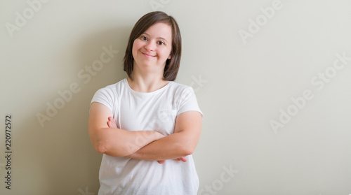 Down syndrome woman standing over wall happy face smiling with crossed arms looking at the camera. Positive person. photo