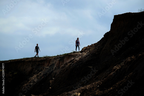 Two people walking near a dangerous clay cliff top.
