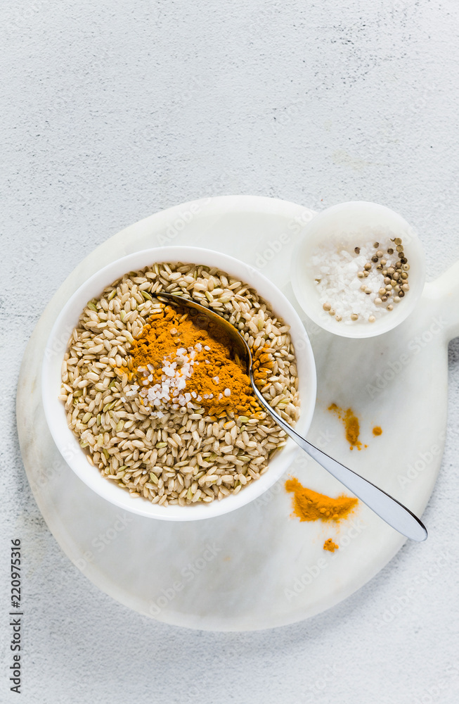 whole-grain rice with turmeric in a bowl on a white marble board. ingredients of a vegan healthy kitchen whole-grain rice with turmeric in a bowl on a white marble board. ingredients of a vegan healthy kitchen