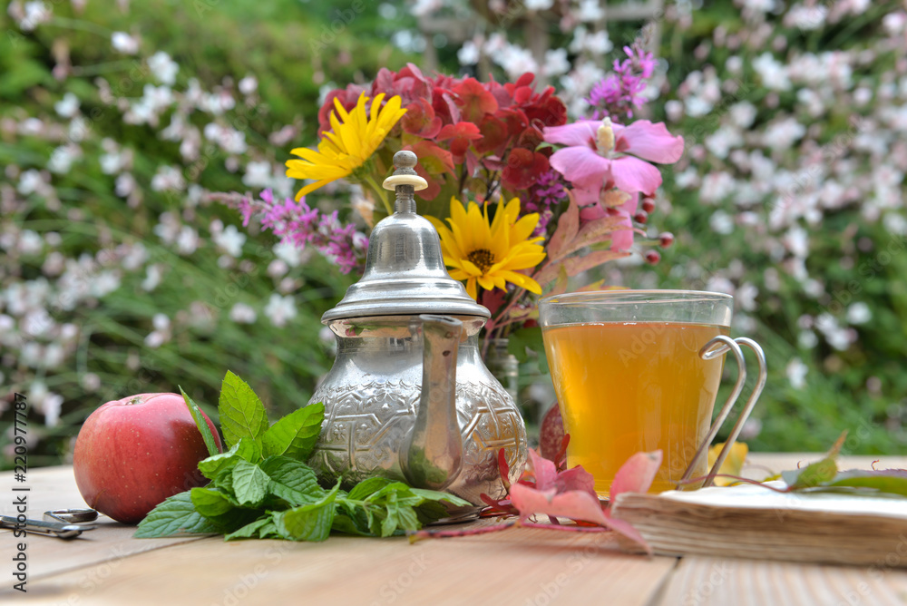 cup of tea on a table with apple and colorful flowers in a garden cup of tea on a table with apple and colorful flowers in a garden