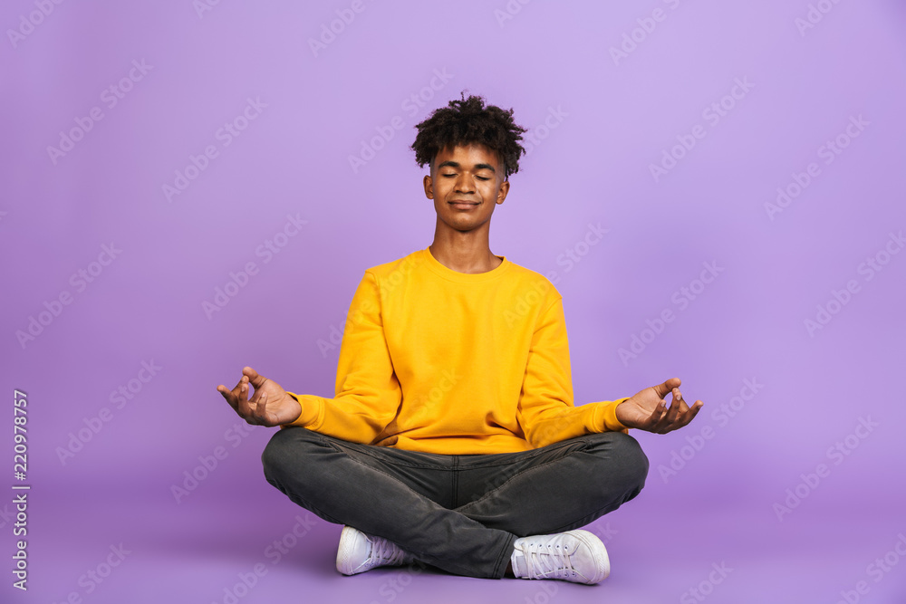 Portrait of relaxed african american boy sitting in lotus pose and meditating with closed eyes, isolated over violet background - obrazy, fototapety, plakaty 
