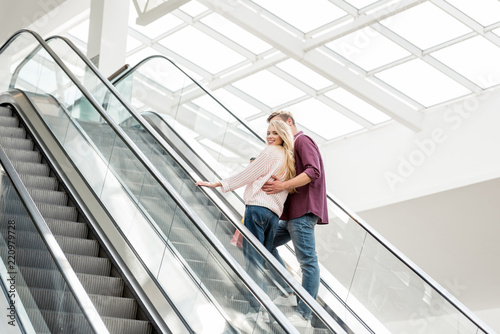 rear view of young couple of shoppers with paper bags on escalator at shopping mall