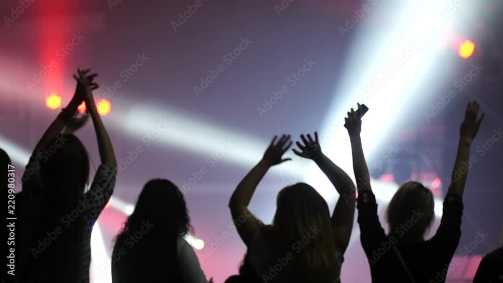 Girl fan silhouettes raise hands dancing enjoying music concert in lumiere light