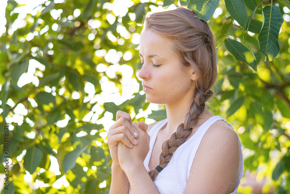 Christian worship and praise. A young woman is praying in the early morning with sun in the background.