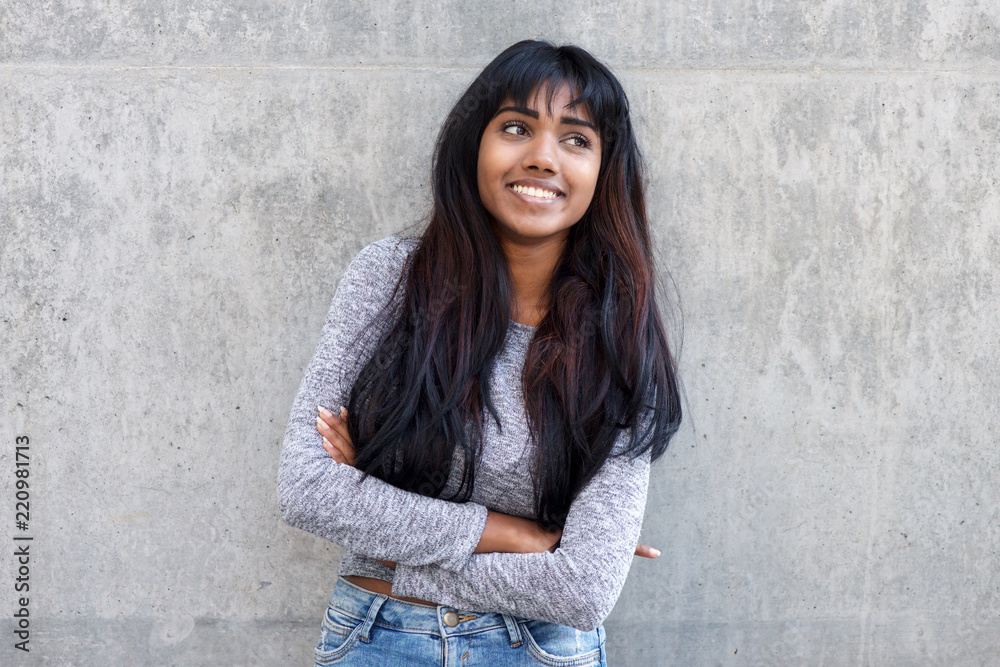happy young Indian woman with arms crossed by gray wall happy young Indian woman with arms crossed by gray wall