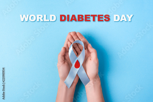 inscription world diabetes day and blue ribbon awareness with red blood drop in woman hands on a blue background