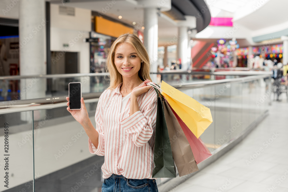 happy young woman with paper bags showing smartphone with blank screen at shopping mall happy young woman with paper bags showing smartphone with blank screen at shopping mall