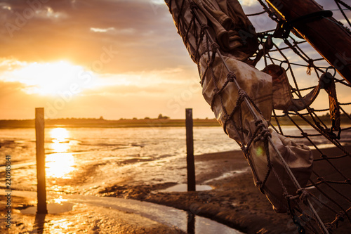 Sail holiday - beautiful sunset at the bottom of the Dutch Waddenzee with big sail boat in foreground